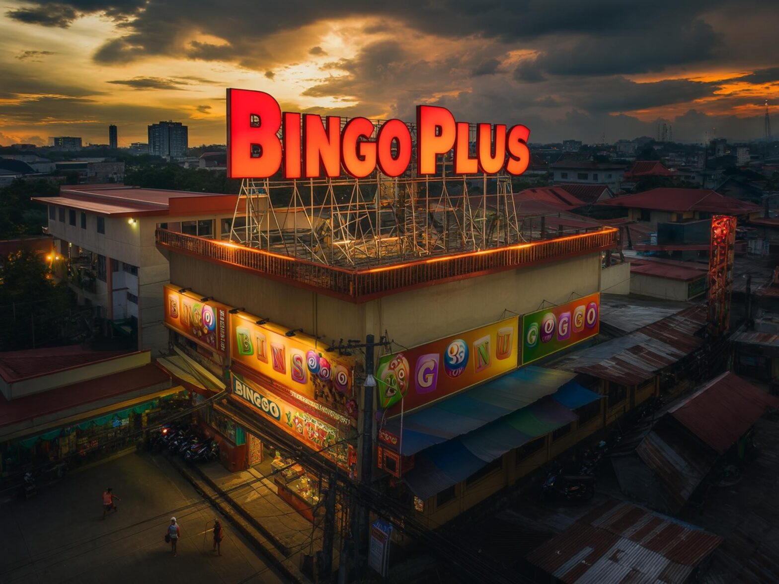 Night view of BingoPlus arcade with illuminated signage and urban landscape in the background under dramatic sunset sky.